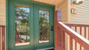 Una puerta verde con una ventana, un letrero con el número 32 y un porche de madera con barandilla roja.
