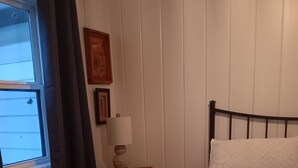 Quarto com cama, mesa de cabeceira, abajur, janela com cortinas e um quadro na parede.