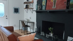 Uma sala de estar com lareira, ventilador de teto, sofá, mesa de centro e televisão na parede.