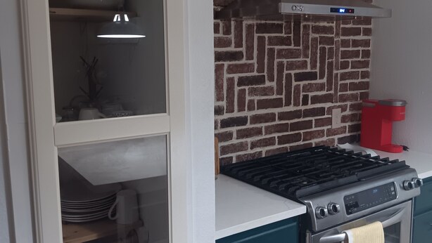 Cozinha com painel de backsplash de tijolos, fogão e armário com portas de vidro.