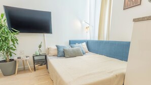 A bedroom with a bed, a TV mounted on the wall, a bedside table with a lamp, a potted plant, and a window with curtains. - Washington by Interhome (Prague centre)