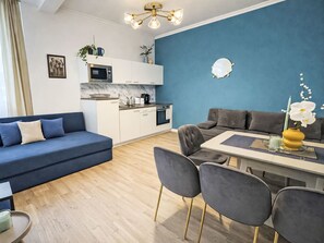Uma sala moderna com uma parede azul de destaque, um sofá, uma mesa de jantar com cadeiras e uma área de cozinha com micro-ondas e armários.