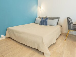 A bedroom with a bed, pillows, a chair, and a wall-mounted light fixture.
