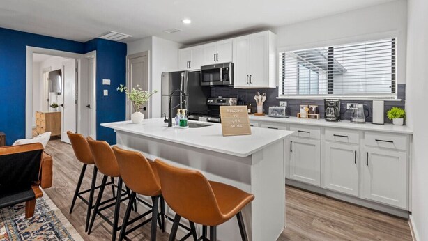 Cocina moderna con armarios blancos, una isla central y taburetes de bar.