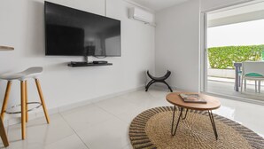Un salon moderne avec un téléviseur à écran plat fixé au mur, une table basse ronde, un tabouret haut et un tapis tissé.