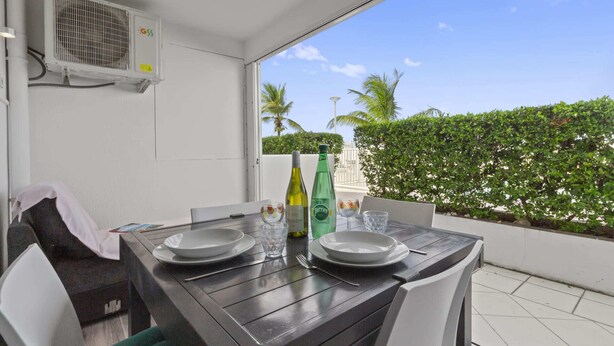 Un balcon avec une table dressée pour deux personnes, une bouteille d’eau Perrier et un verre. Un appareil de climatisation blanc est fixé au mur.