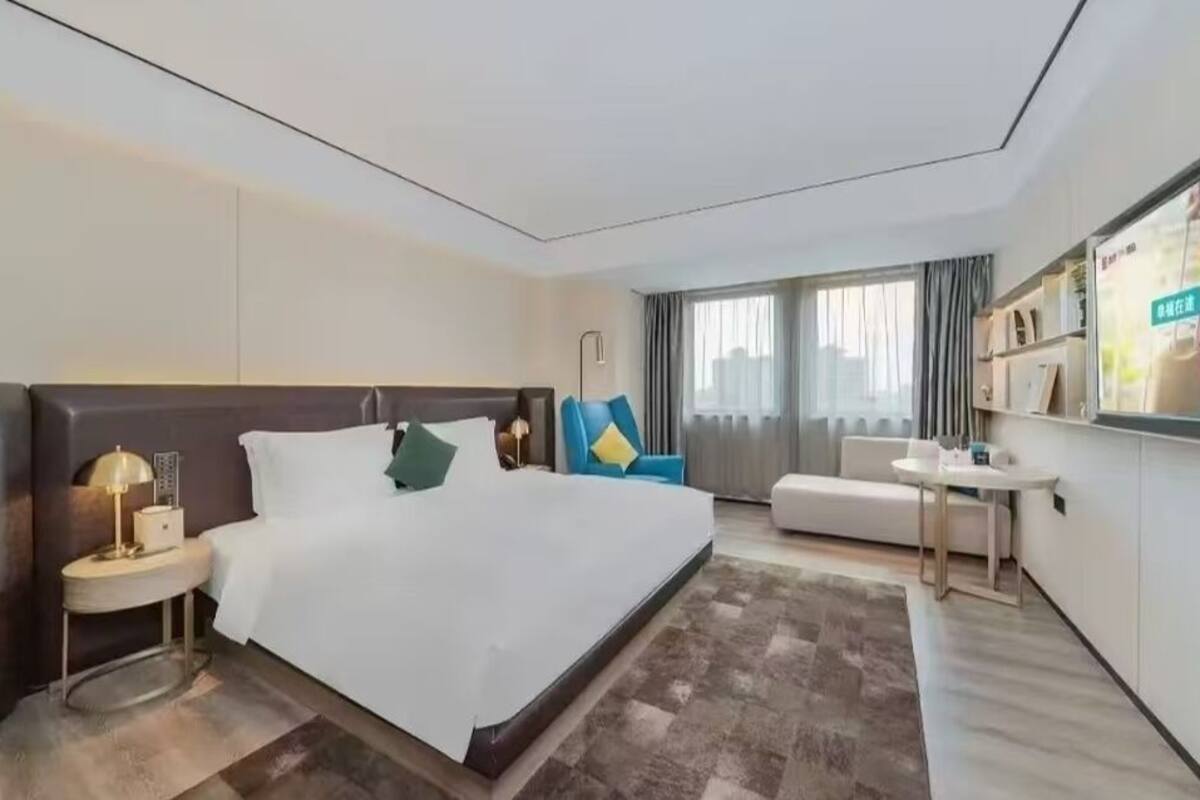 Una camera d'albergo con un letto grande, un comodino con una lampada, un tavolino piccolo e rotondo, un divano e una TV montata a parete.