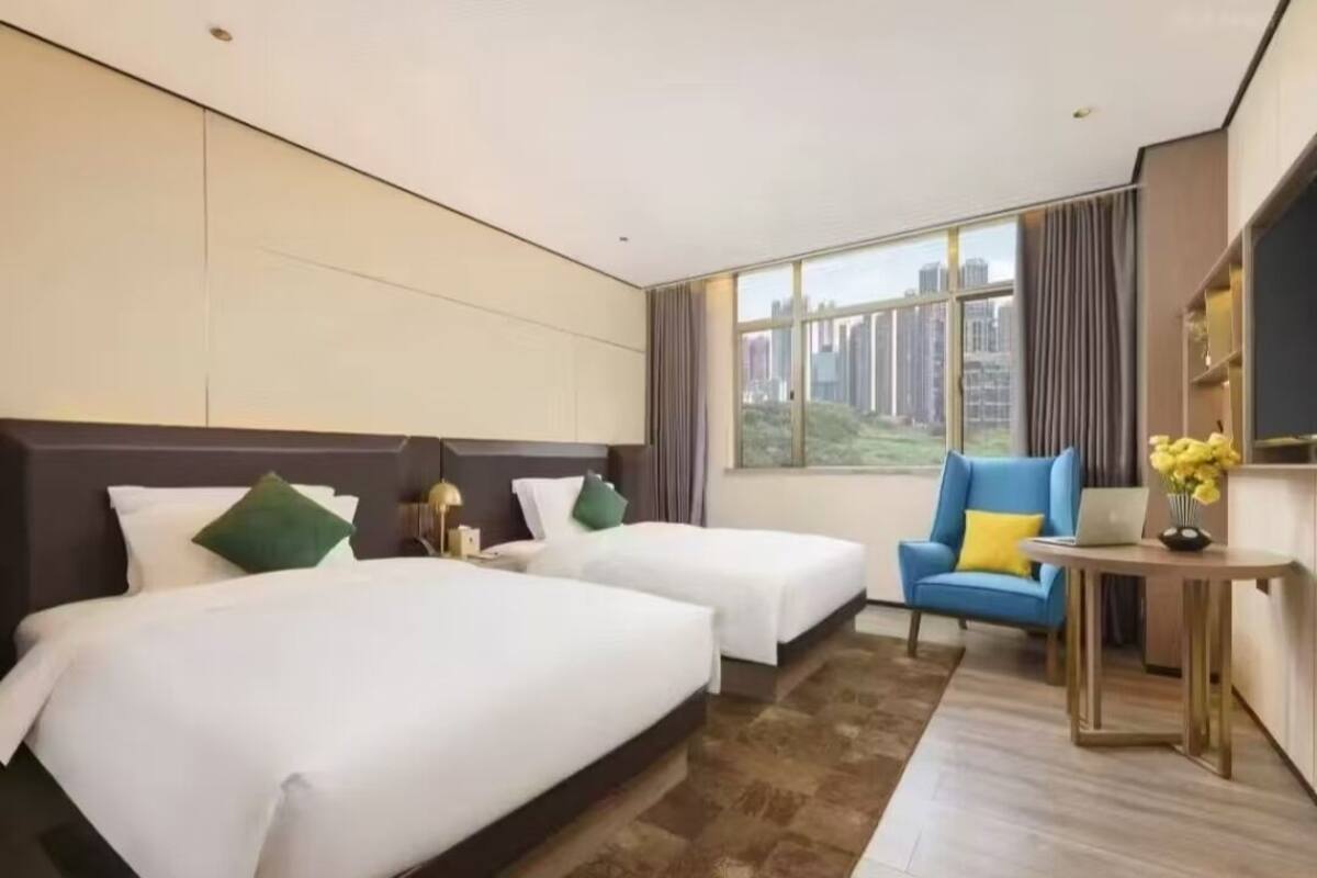 Camera d'albergo con due letti, una scrivania, una sedia e un'ampia finestra che si affaccia sulla città.