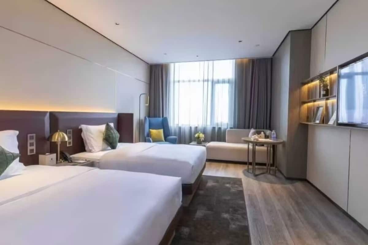Una camera d'albergo moderna con due letti, un tavolino, una poltrona e una televisione.
