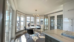 A spacious kitchen with large windows, a round dining table, and modern black chairs. - Luxury Riverside Villa with Magnificent RiverViews (Laval)