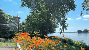 A waterfront park with orange flowers, a lamp post, and a tree. - Luxury Riverside Villa with Magnificent RiverViews (Laval)