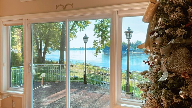 A room with large windows overlooking a lake, a balcony with a railing, and a decorative wall. - Luxury Riverside Villa with Magnificent RiverViews (Laval)