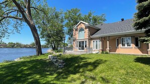 A house with a large window, a stone wall, and a lawn. - Luxury Riverside Villa with Magnificent RiverViews (Laval)
