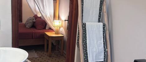 A bathroom with a sink, a mirror, a wooden door, a tiled floor, and a small table with a lamp.