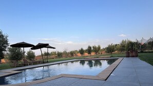 A swimming pool with a tiled deck, two umbrellas, and potted plants. - A haven of peace in Marrakech (Marrakech)