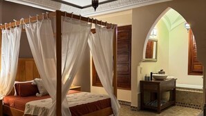 A four-poster bed with a canopy, a small bedside table with a lamp, and a view of a tiled bathroom through an arched doorway. - A haven of peace in Marrakech (Marrakech)