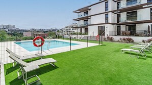 Ein modernes Gebäude mit Pool auf dem Dach, einer grünen Rasenfläche und Liegestühlen.