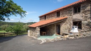 Un bâtiment en pierre avec un toit en tuiles, un banc en bois à l’extérieur et une vue sur un paysage verdoyant.
