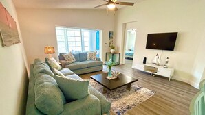 A living room with a sectional sofa, a coffee table, a TV, and a small white cabinet.