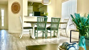 A dining area with a wooden table and chairs, a hanging light fixture, and a window with blinds.
