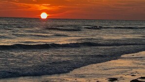 A sunset over the ocean with waves approaching the shore.