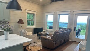 A spacious living area with a large window, a sofa, a TV, and a dining table. - Romantic Getaway at Honeymoon Cottage (Pisgah)