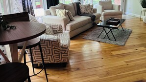 A living room with a beige sofa, patterned ottoman, and a small round table. - Serenity by the Lake. Spacious lake house incredible views in Colonial Beach (Colonial Beach)