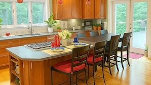 A kitchen with wooden cabinets, a large island with chairs, a stove, and a window overlooking greenery. - Serenity by the Lake. Spacious lake house incredible views in Colonial Beach (Colonial Beach)