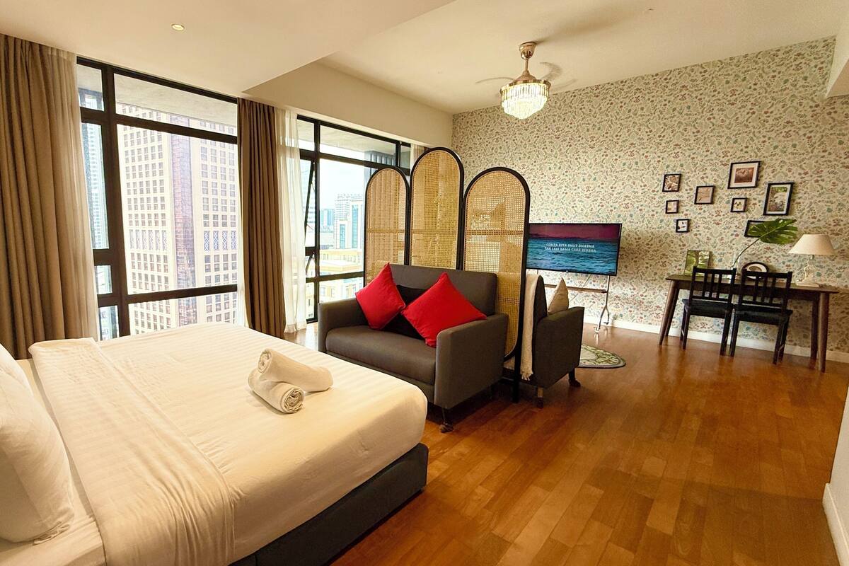 Habitación de hotel con una cama grande, un sofá, un televisor y vistas a la ciudad a través de las ventanas.