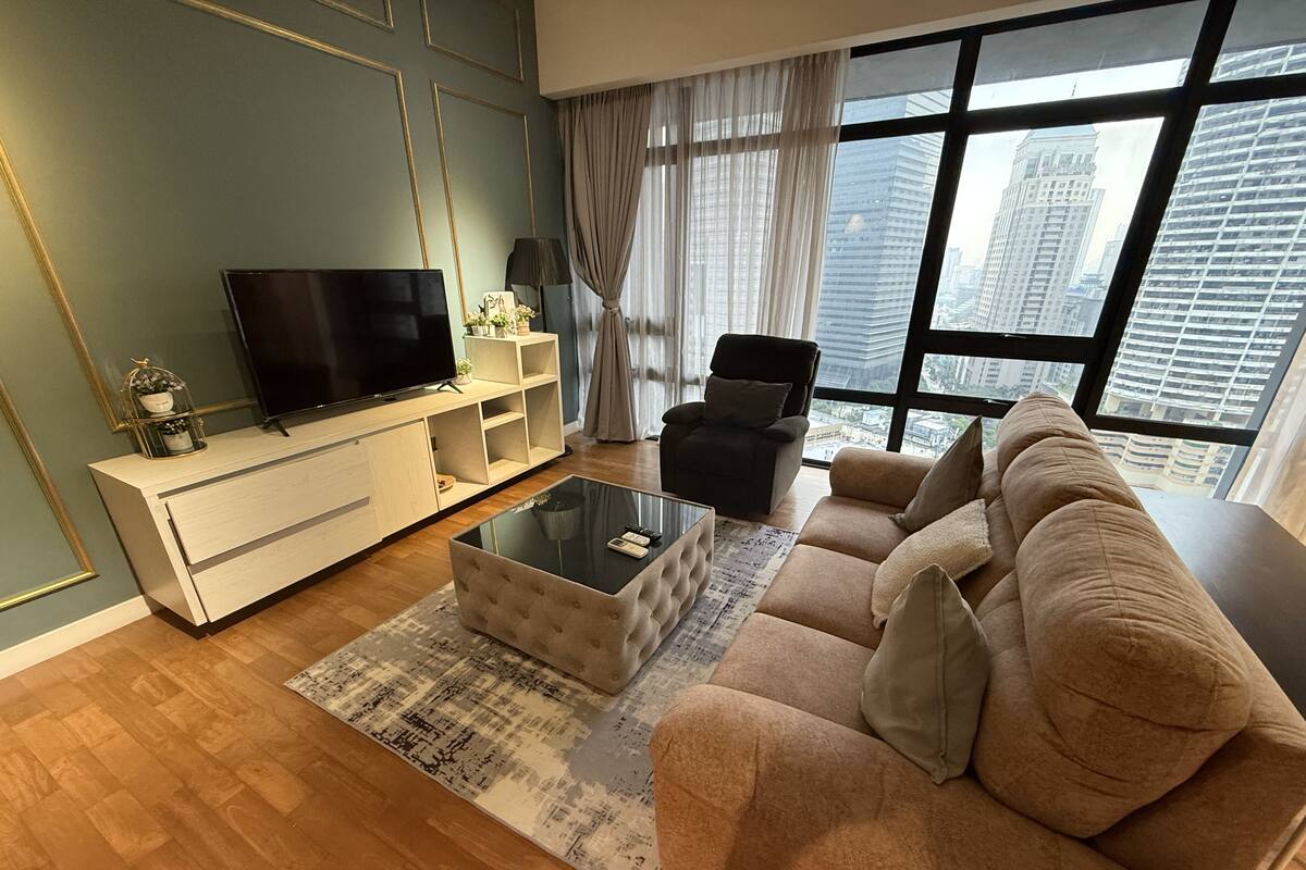 Una sala de estar moderna con un televisor de pantalla plana, un sofá, una mesa de centro y un ventanal con vistas a la ciudad.