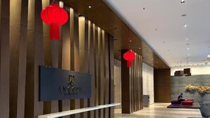 A modern hotel lobby with a wooden reception desk, red hanging lanterns, and a sign reading "ANGELUN HOTEL".