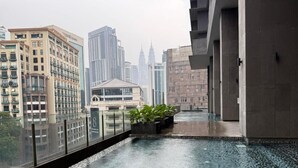 A modern building with a glass balcony, a wet floor indicating recent rain, and a view of city skyscrapers in the background.