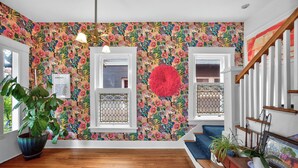 A room with wooden flooring, a large potted plant, a blue rug, a red spherical decoration, and a staircase with white railings. - Walk to 5 Points • 2 Living Areas • Game Room + Gym (Nashville)