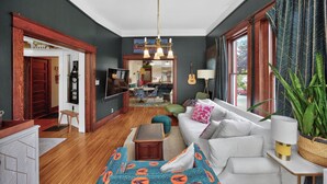 A living room with a sofa, a television, a dining area, and a kitchen in the background. - Walk to 5 Points • 2 Living Areas • Game Room + Gym (Nashville)