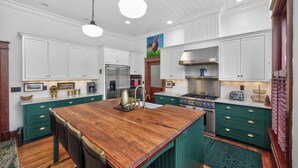 A kitchen with white cabinetry, a wooden island, stainless steel appliances, and a green accent wall. - Walk to 5 Points • 2 Living Areas • Game Room + Gym (Nashville)