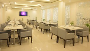 Un restaurant moderne doté de plusieurs tables et chaises, d’un téléviseur à écran plat fixé au mur et de panneaux décoratifs aux fenêtres.