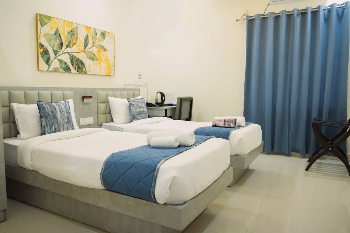 A hotel room with two beds, a desk, a chair, a coffee maker, and a painting on the wall.