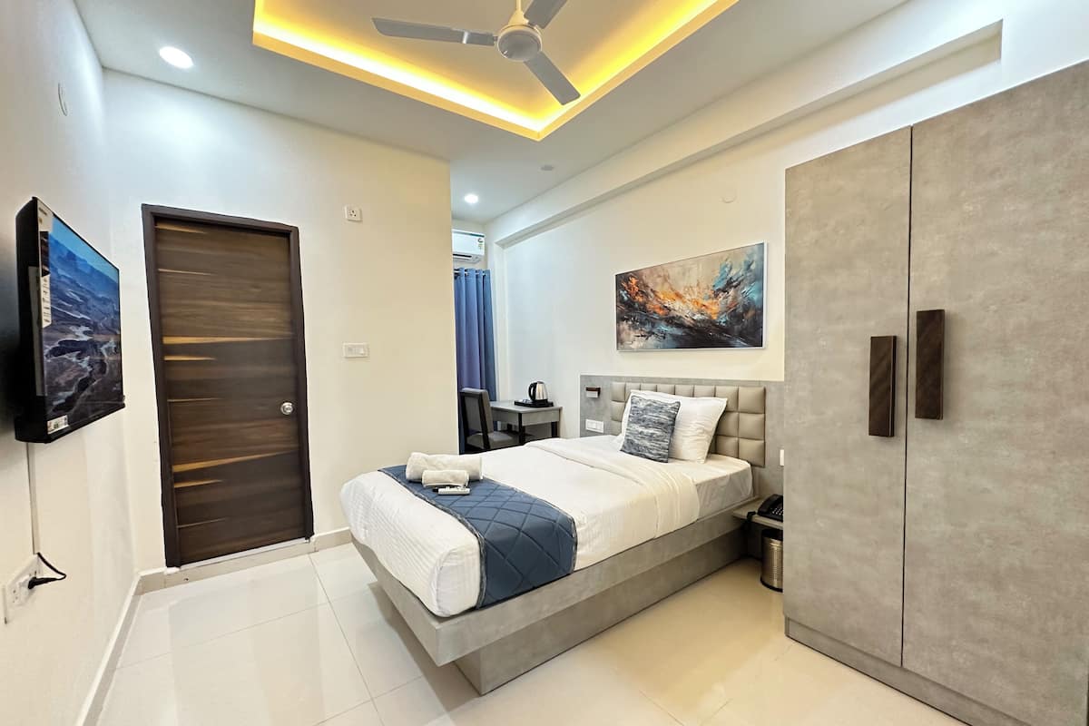A modern bedroom with a bed, a wardrobe, a ceiling fan, a TV, and a painting on the wall.