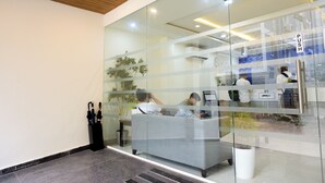Un espace d’accueil doté d’une cloison en verre, d’un comptoir de réception, d’un coin salon et d’une plante.