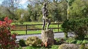 A statue of a figure with a child in a park setting.