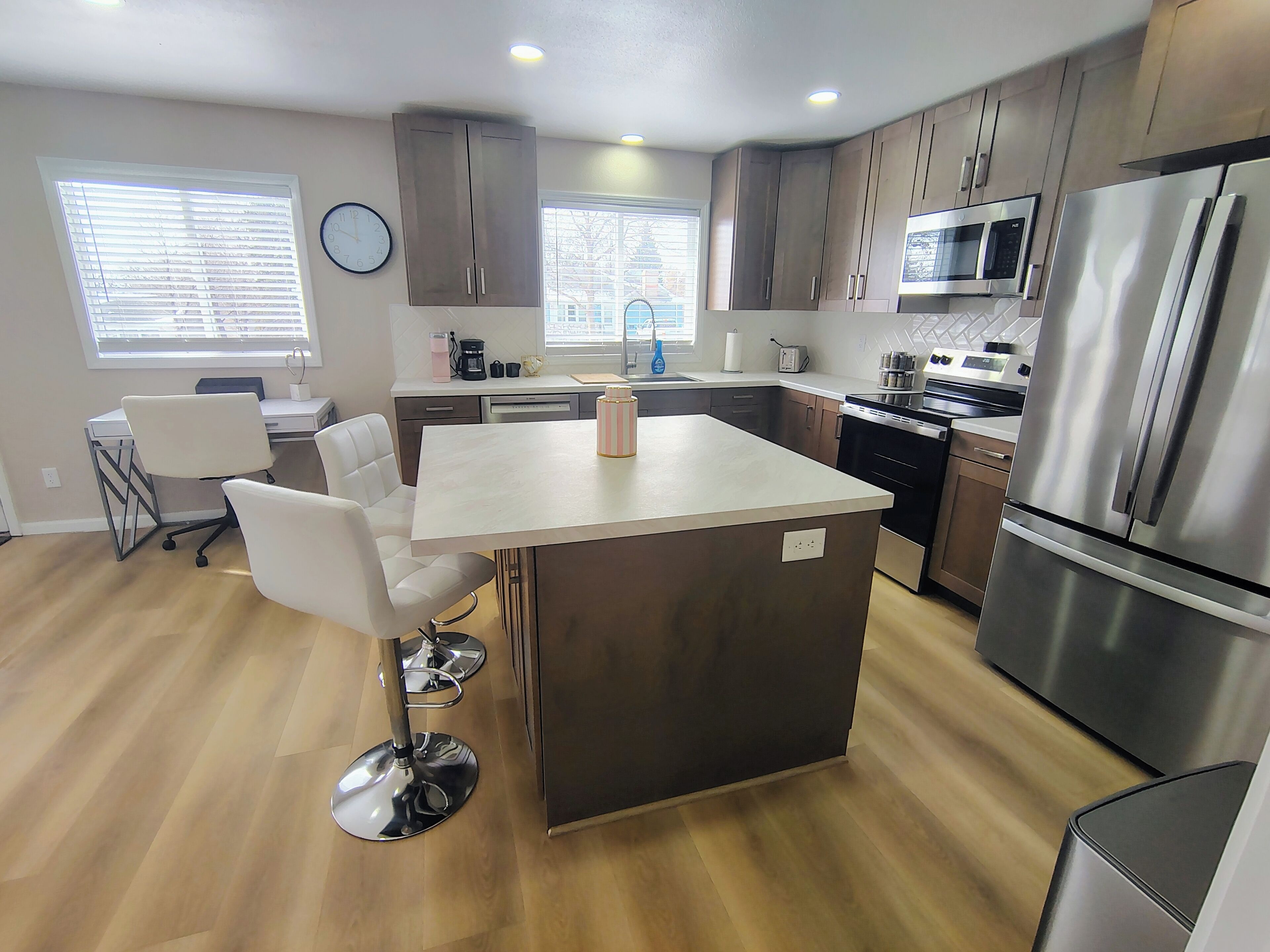 A modern kitchen with a central island, stainless steel appliances, and a dining area with white chairs.