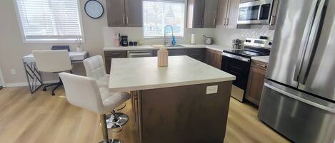A modern kitchen with a central island, stainless steel appliances, and a dining area with white chairs.