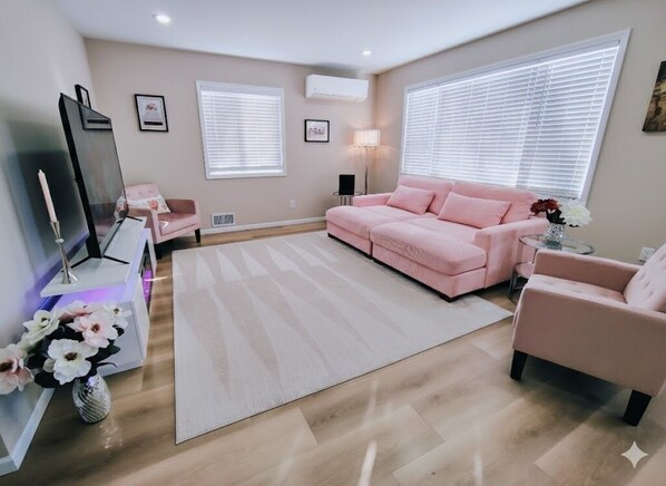 A modern living room with a pink sofa, a TV, and a decorative vase with flowers.