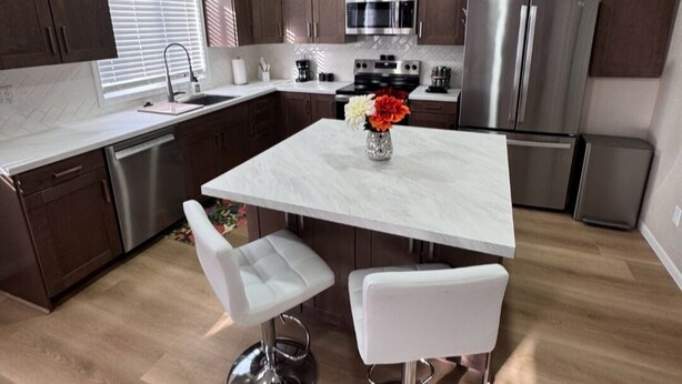 A modern kitchen with dark wood cabinets, stainless steel appliances, a marble island, and white bar stools.
