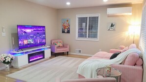 A living room with a flat-screen TV, pink furniture, a white rug, and a window with blinds.