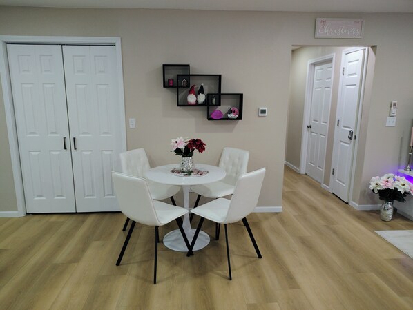 A dining area with a round table and four white chairs, a vase with flowers, and a wall-mounted shelf with decorative items. - Centrally Located 2 King Bed 2 Bath (Bismarck)