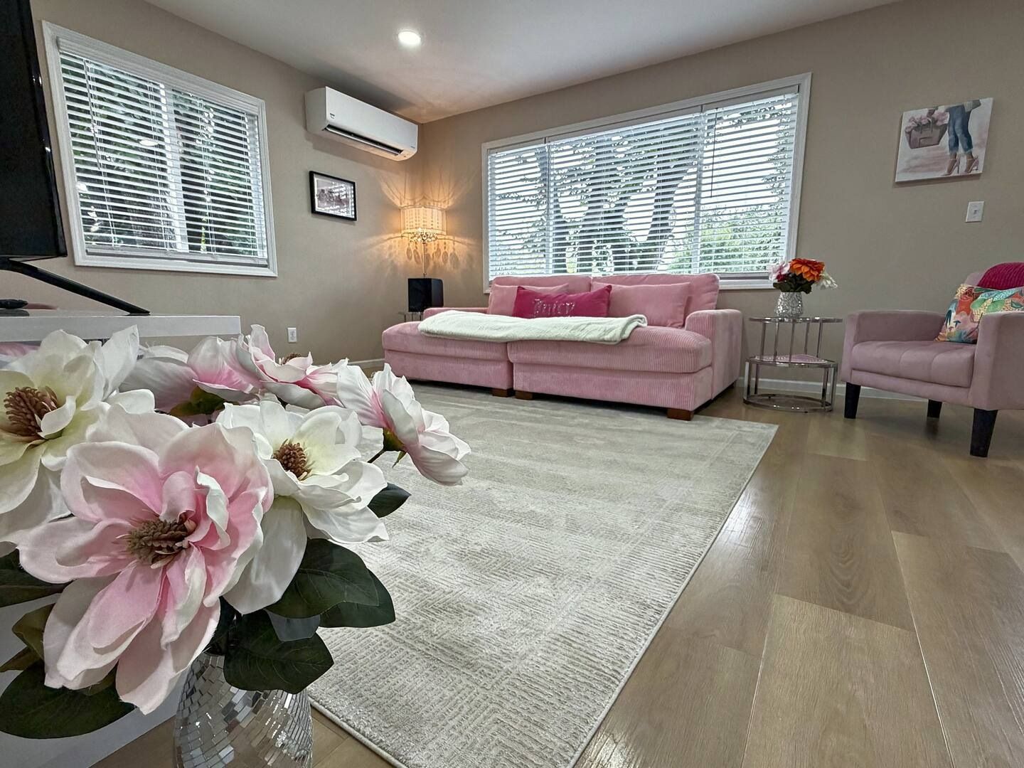 A living room with a pink sofa, a coffee table, a rug, and large artificial flowers.