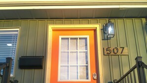 A house with a bright orange door, a mailbox, and a number sign '507' on the wall.
