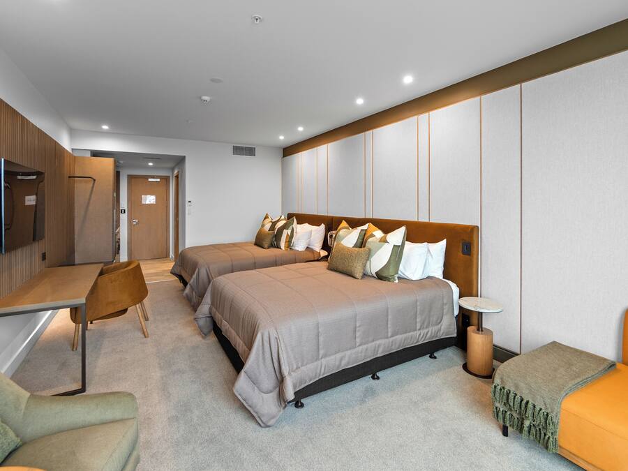 A modern hotel room with two beds, a desk, a chair, and a small table.