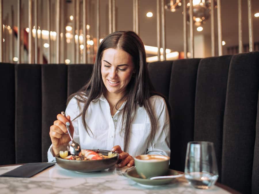 A person seated at a table with a bowl of food and a cup of coffee, in a restaurant with a modern interior and dark seating.